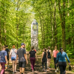 A group of about ten people are walking on a dirt path through a forest. They are all wearing athletic clothing and carrying water bottles
